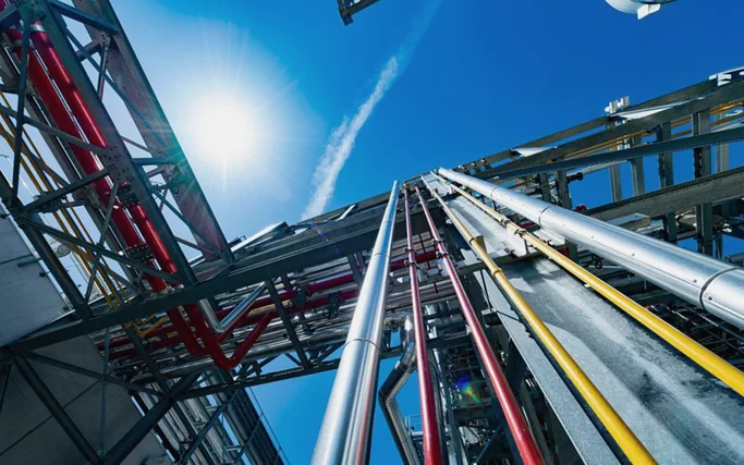 Upward view of converging industrial pipework against a clear sky